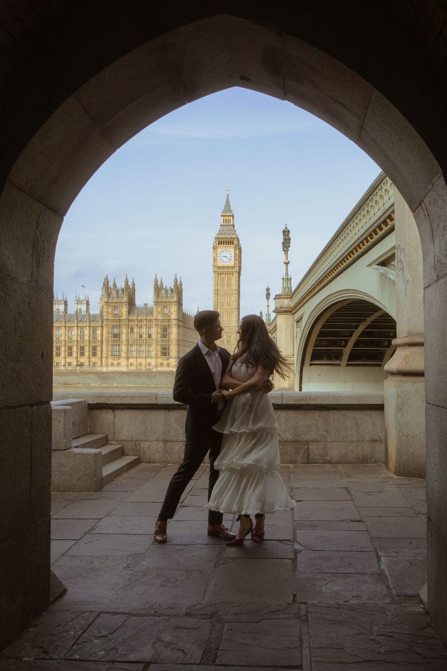 Couple dancing under a stone archway with Big Ben and the Houses of Parliament in the background in London.
