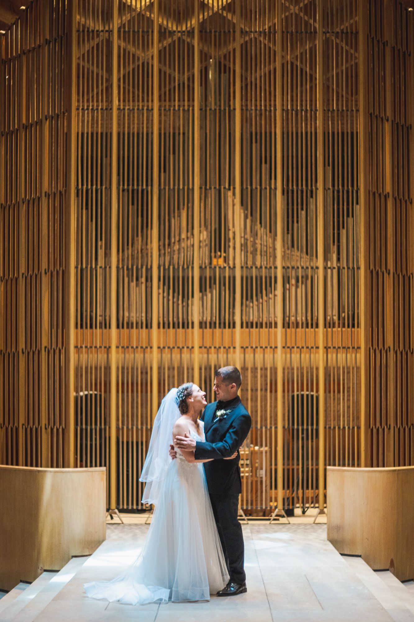 A couple shares an intimate moment before tall golden organ pipes in an elegant chapel during their wedding ceremony.
