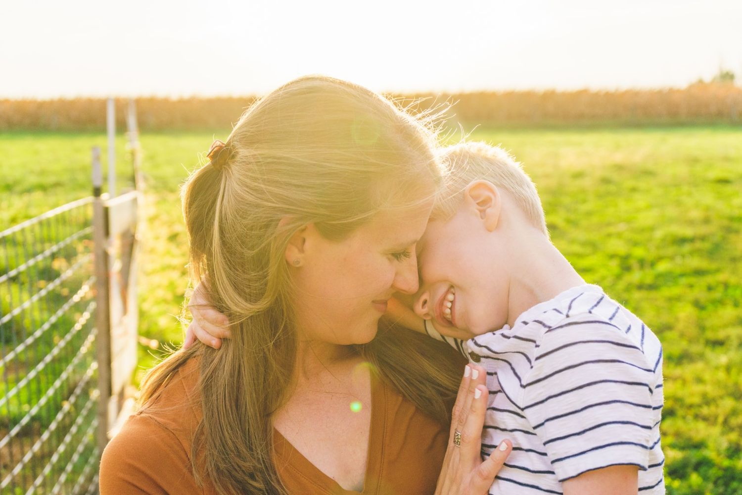 A tender mother-child moment backlit by golden sunlight in a grassy field.