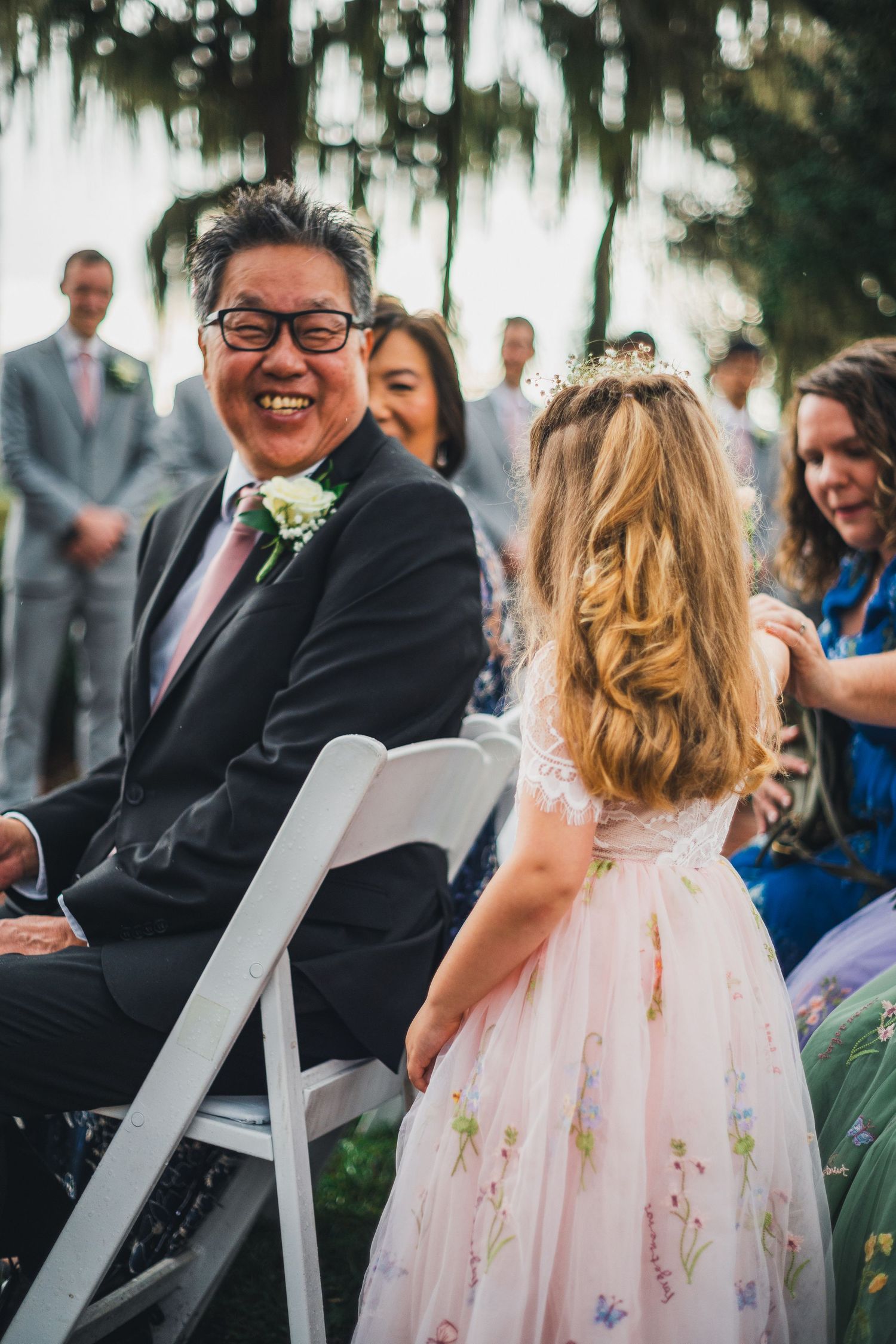 A heartwarming moment at an outdoor wedding ceremony with guests smiling and a child in a pink floral dress.