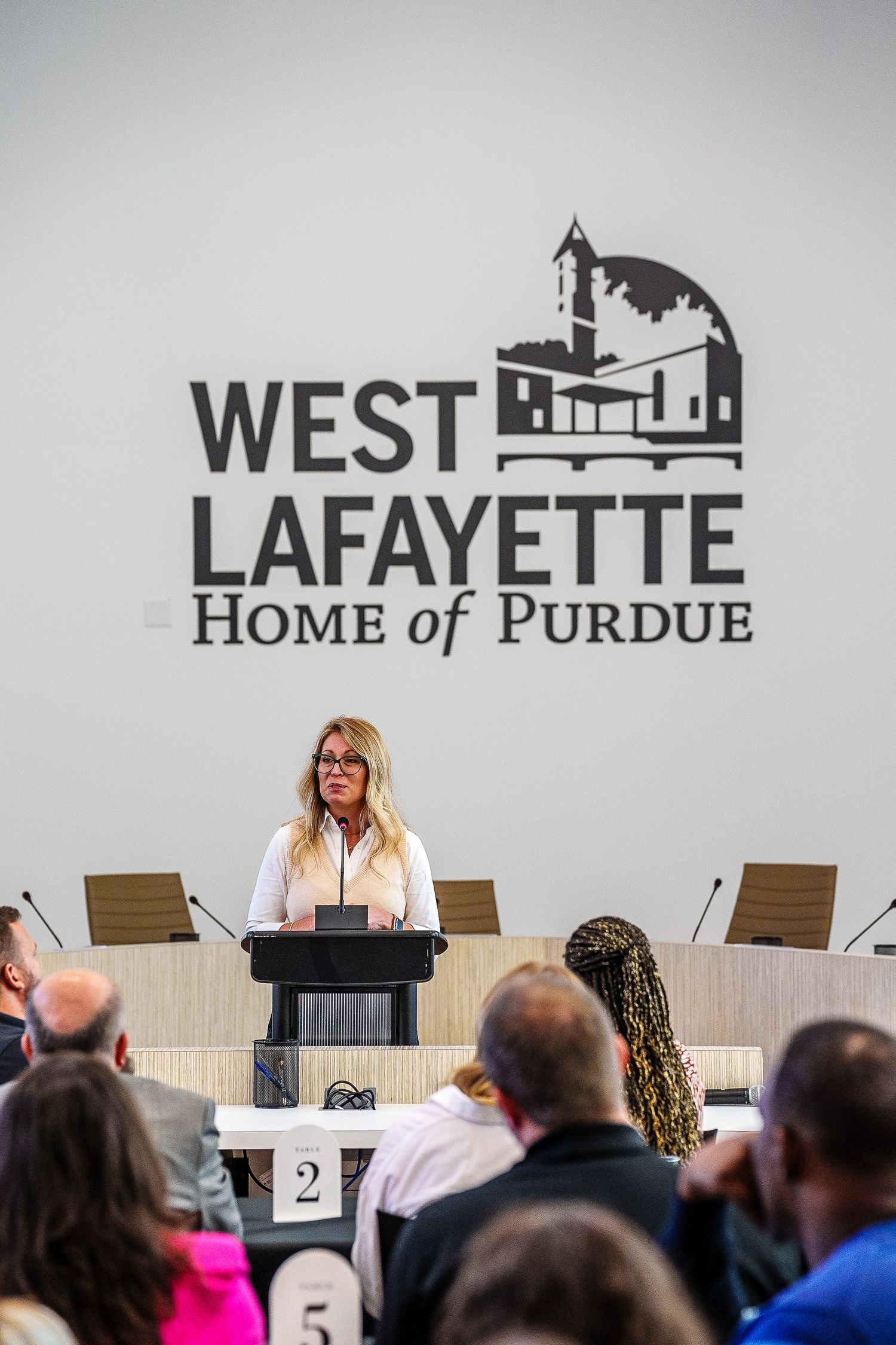 A speaker stands at a podium during a presentation under a West Lafayette Home of Purdue logo and signage.