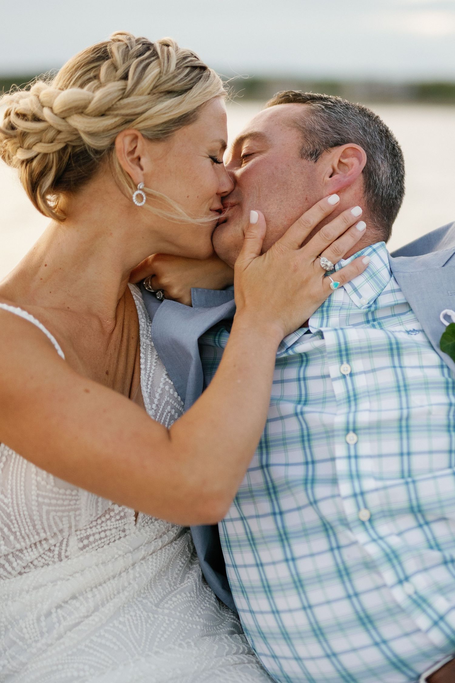 A romantic kiss between a couple on their wedding day, with the bride wearing a white dress and braided updo hairstyle.
