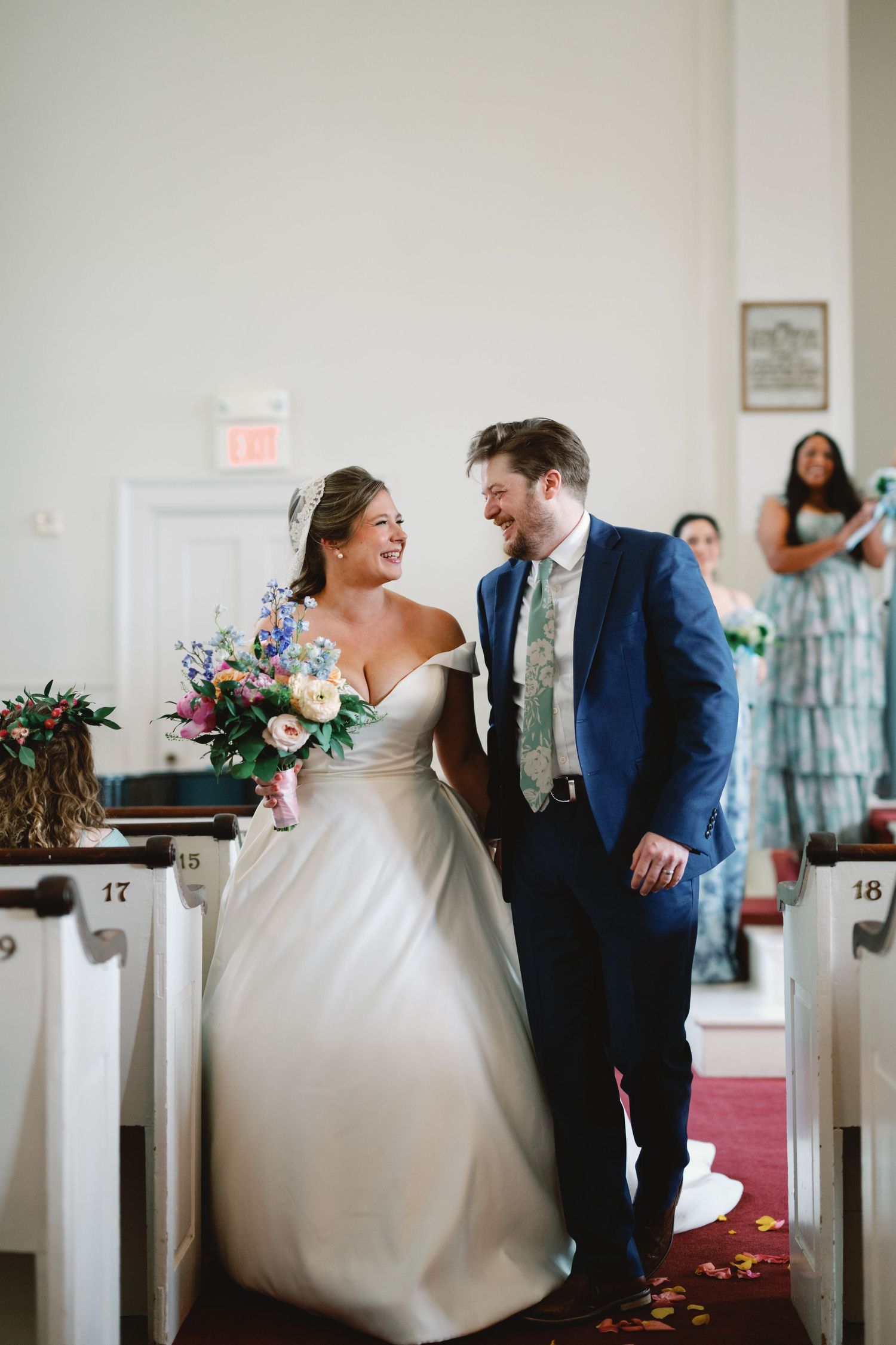 A bride and groom laugh together while walking down the church aisle after their wedding ceremony.