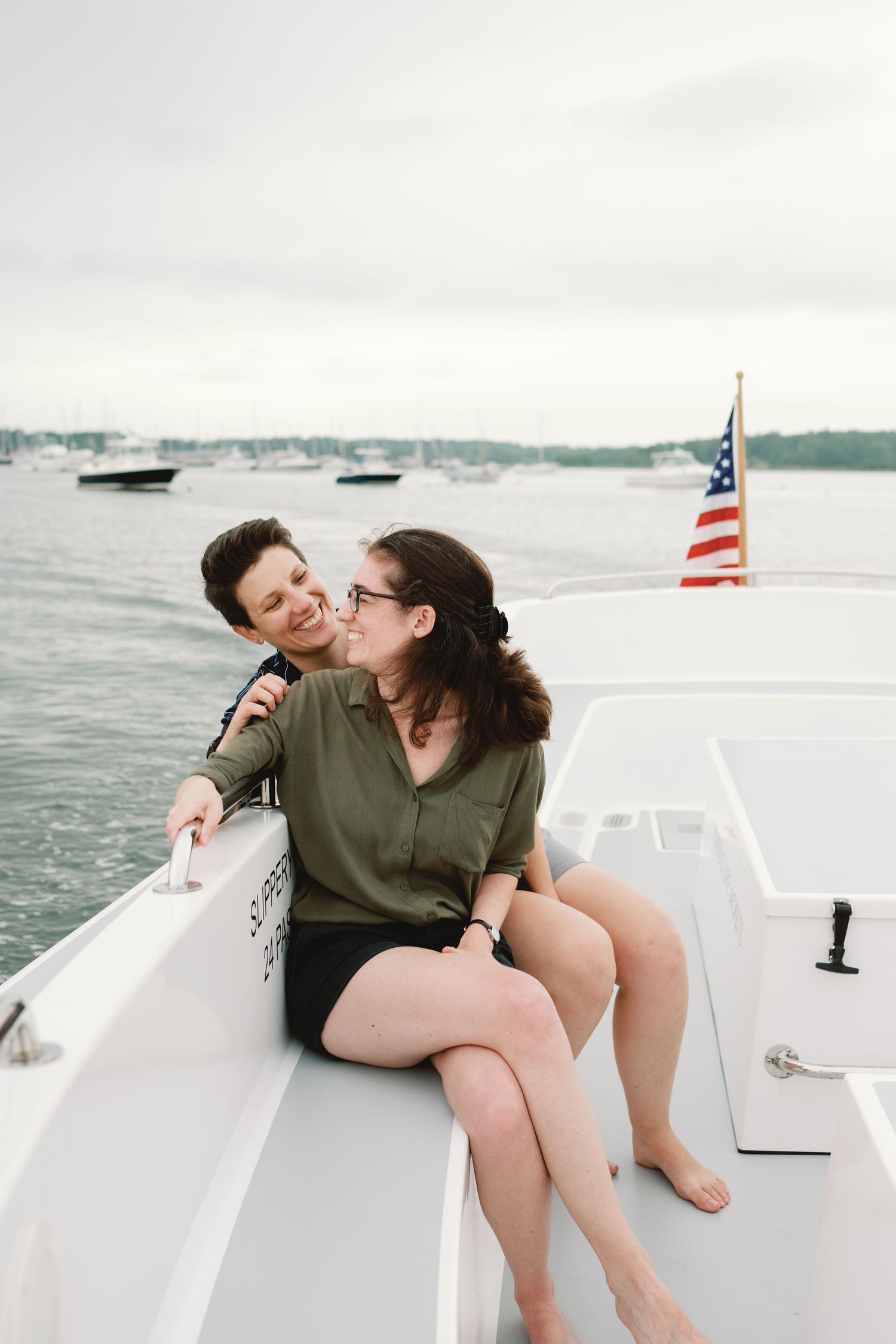 A couple shares a tender moment while sitting on the bow of a boat with an American flag in the background.