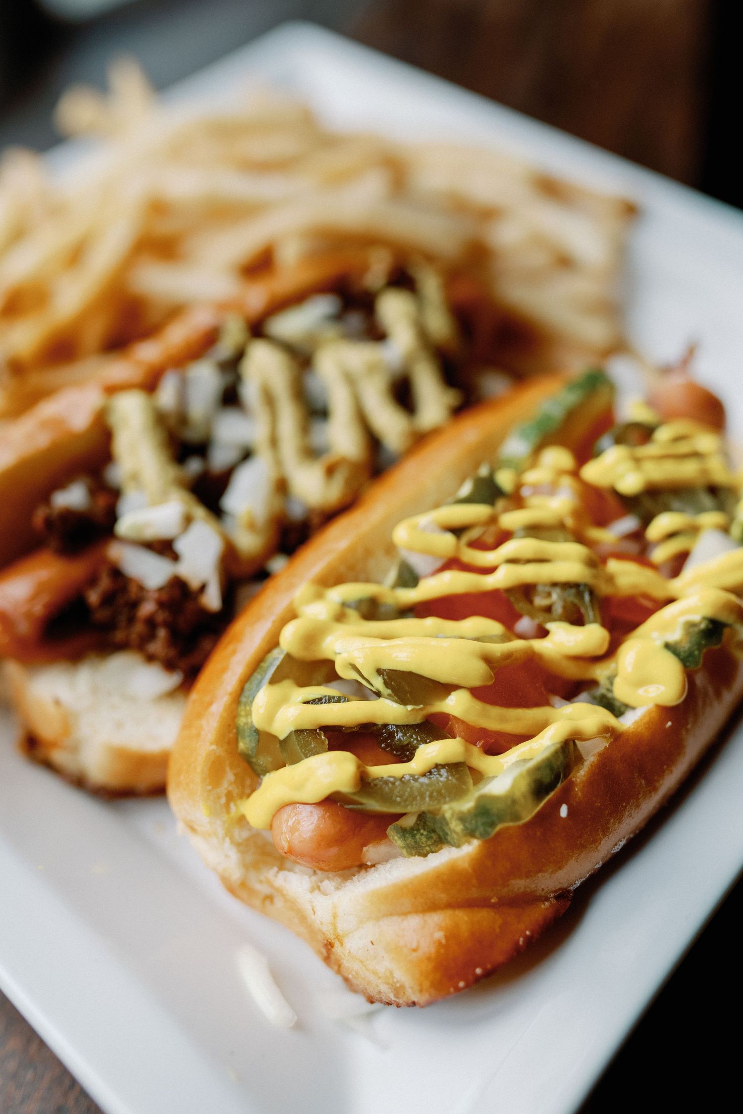 A hot dog topped with mustard, onions and jalapenos on a toasted bun shown in close-up detail.
