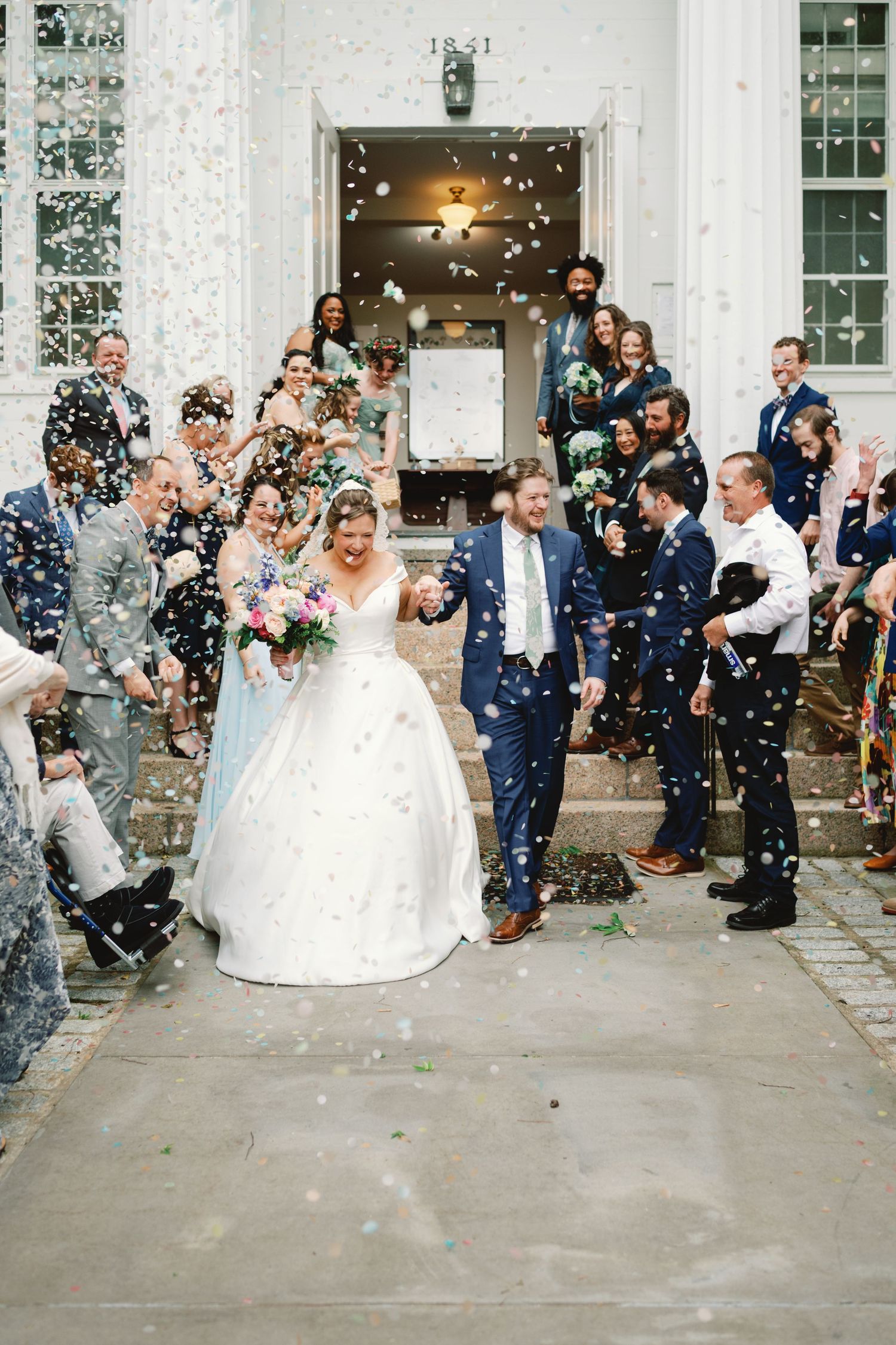 Wedding guests shower a newly married couple with confetti on church steps during their joyful celebration exit.
