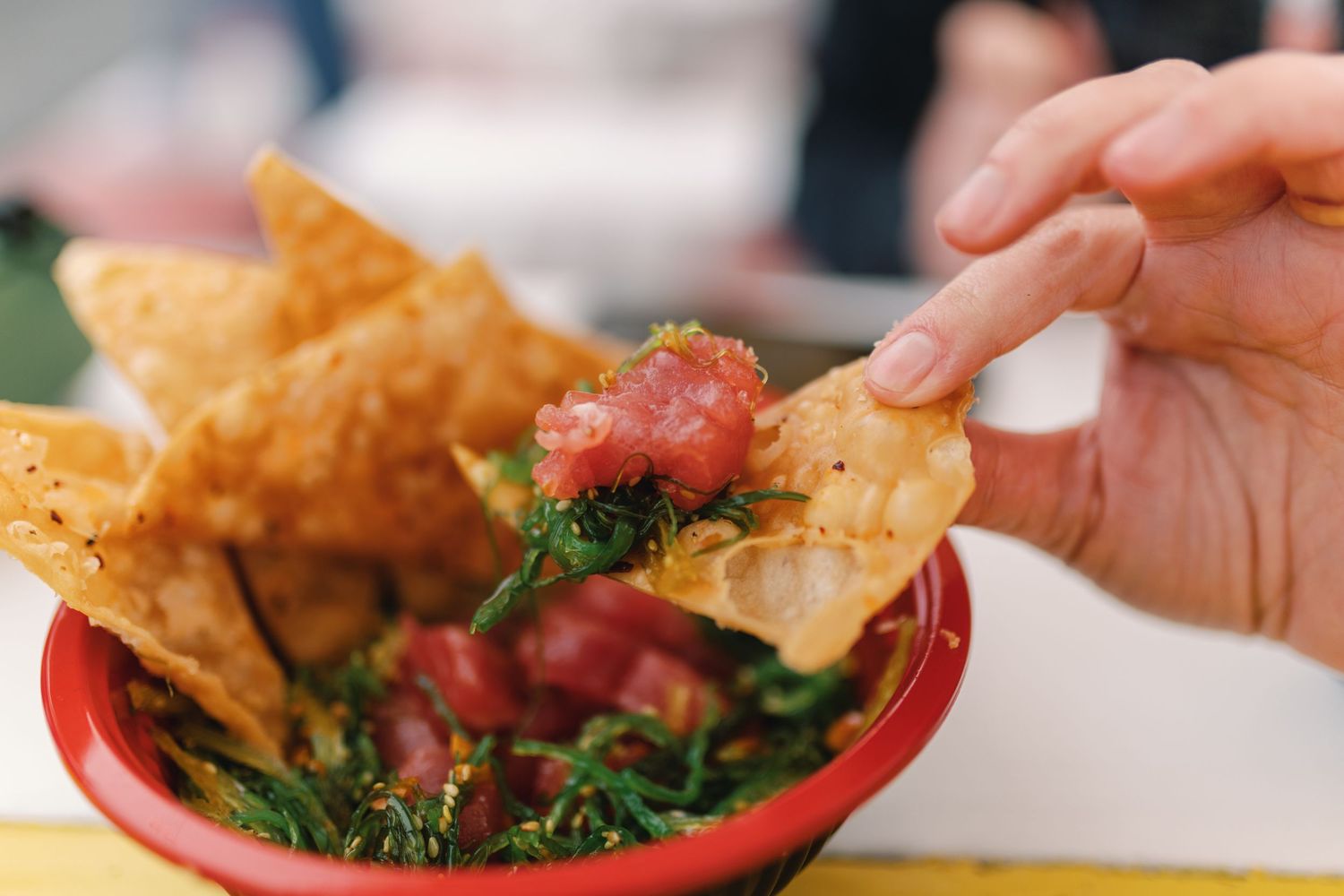 Hands reaching for crispy fried appetizers with dipping sauce served in red bowls on a white table.