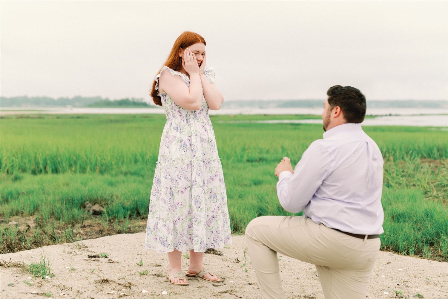 A marriage proposal takes place on a path overlooking green marshland on a misty day.