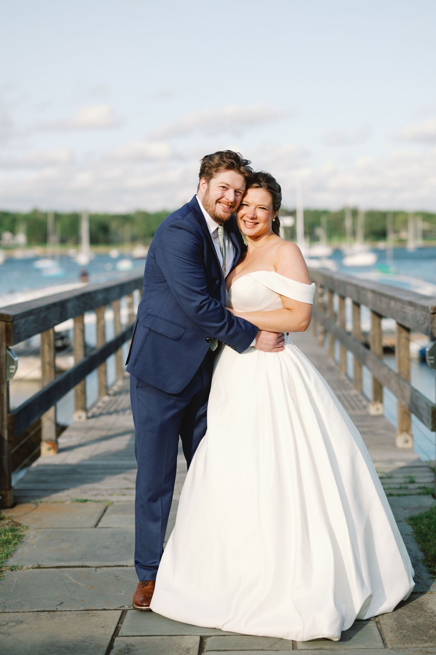 A couple poses romantically on a wooden dock by the water during their waterfront wedding celebration.