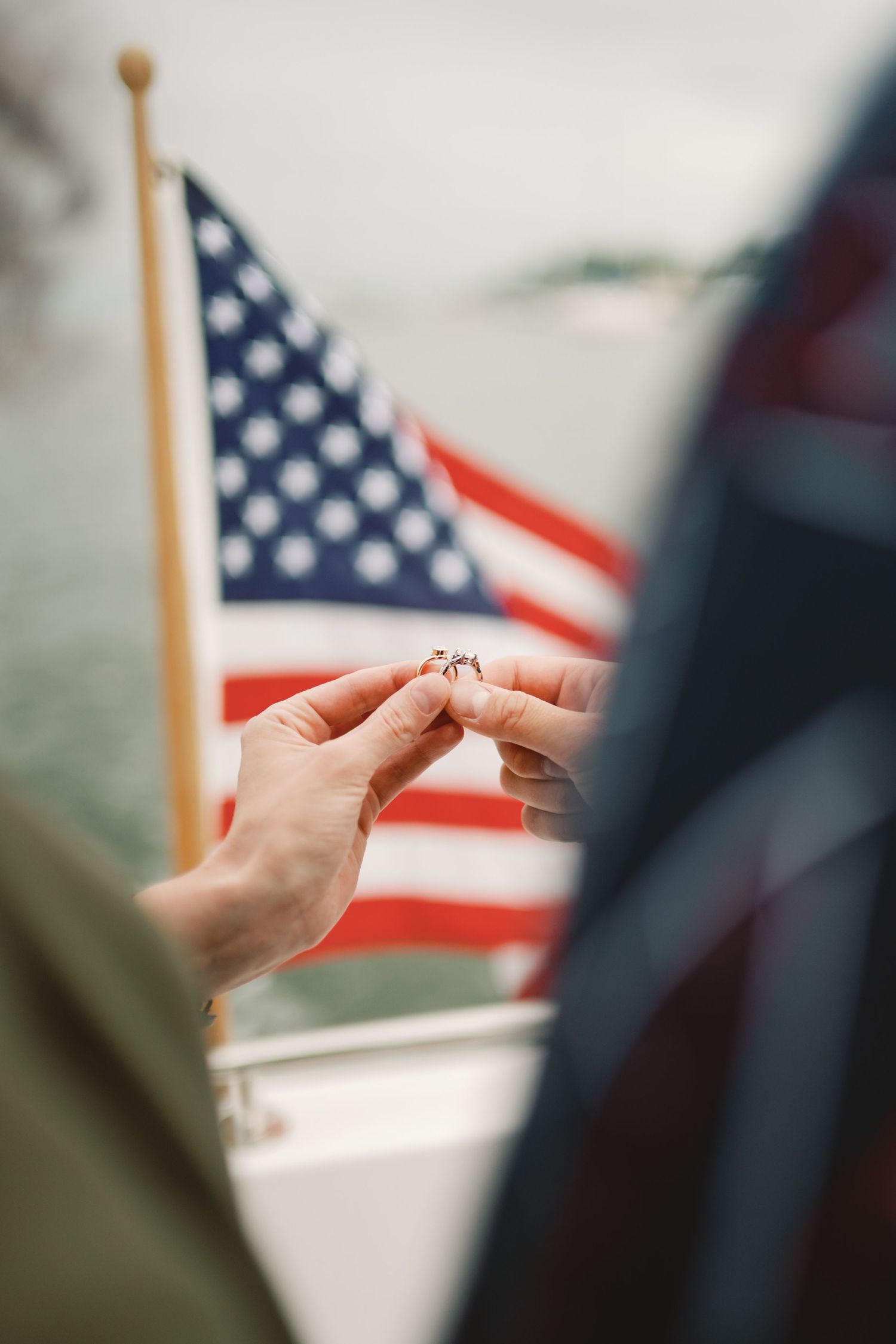 Person holding their hand in a heart shape gesture with an American flag visible in the background.
