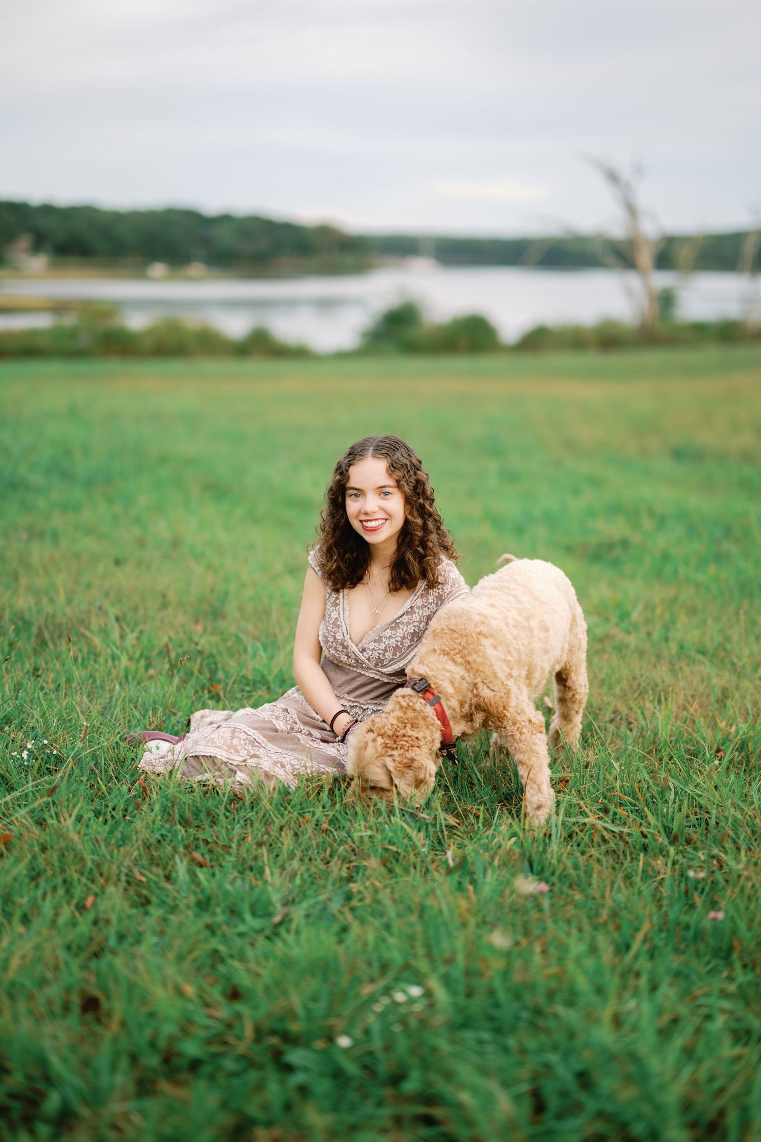 A person in a floral dress plays in a green field with a golden retriever dog on a sunny day.