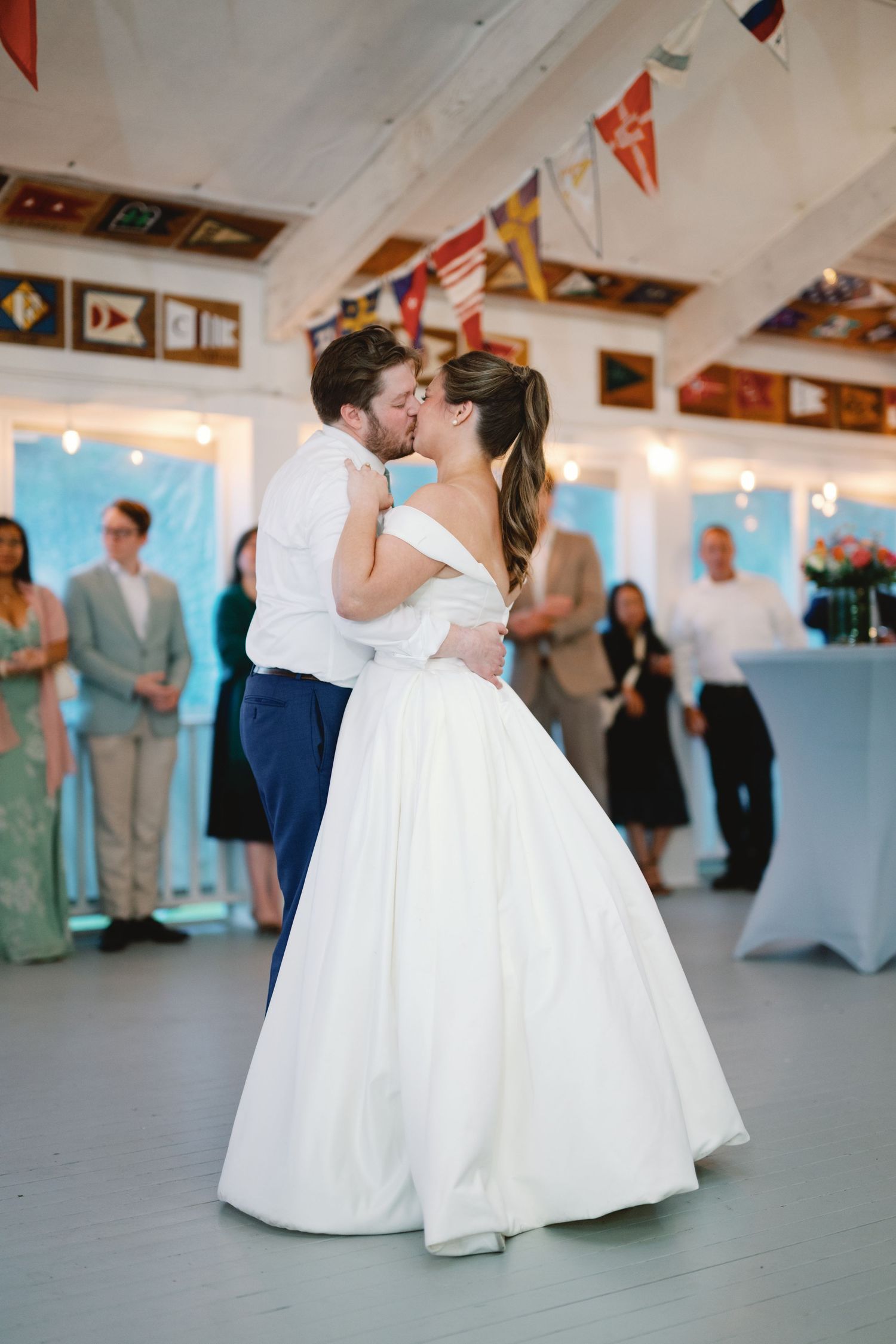 A couple shares their first dance at a wedding reception under colorful flag bunting and twinkling lights.