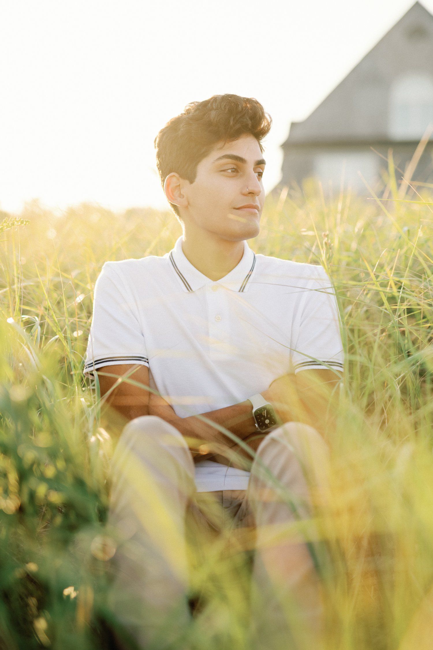 Person in white polo shirt sitting in tall grass during golden hour sunset.