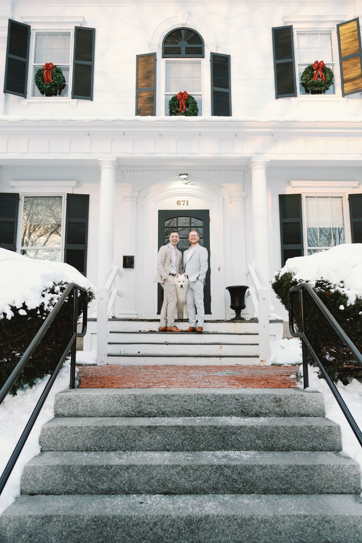 White colonial building entrance with granite steps and decorative holiday wreaths adorning arched windows.