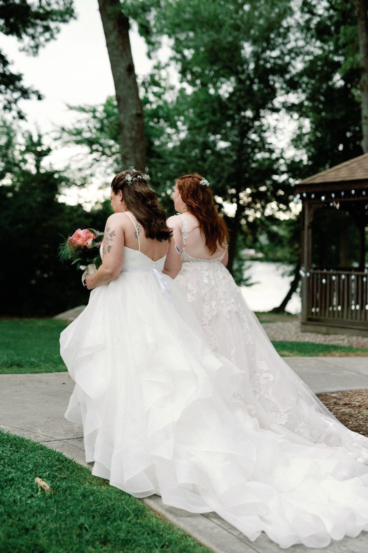 Three figures in flowing white bridal gowns sit together on a porch step in an outdoor garden setting.
