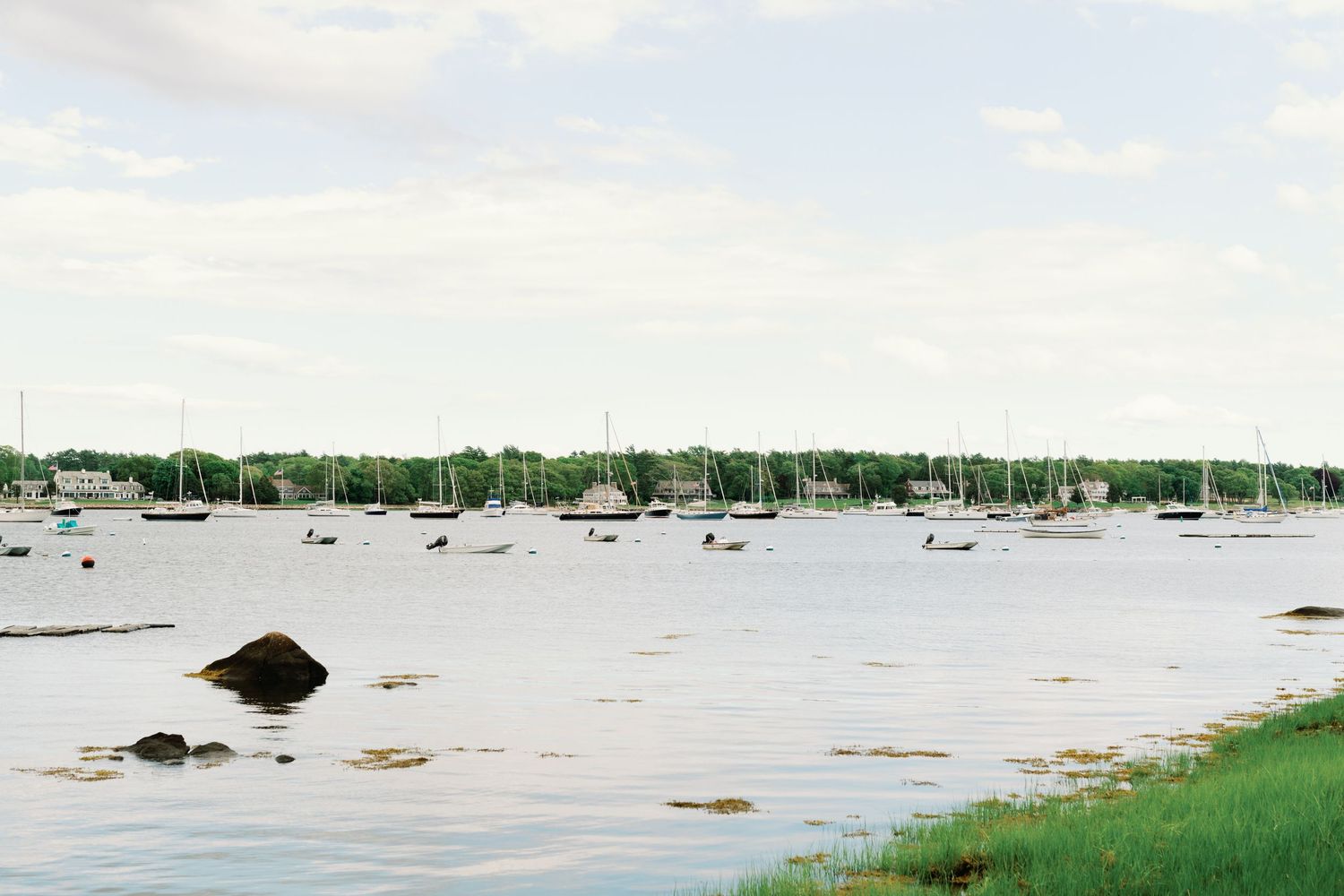 Five panoramic photos of a coastal area with boats on tranquil waters near grassy shorelines and mudflats during low tide.