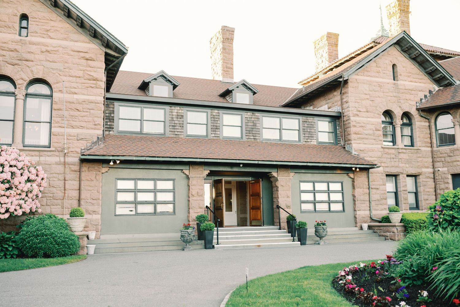 Victorian-style mansion with brown sandstone exterior, dual garages, and landscaped garden entrance in daylight.