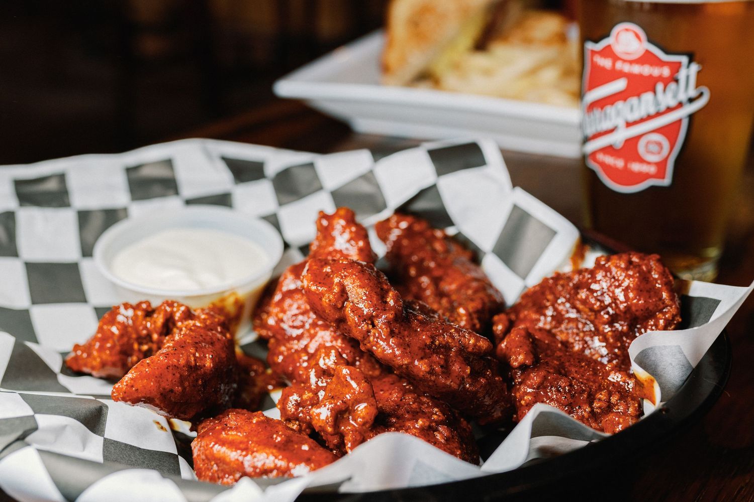 Spicy buffalo chicken wings served on checkered paper with ranch dipping sauce and a soda can in the background.