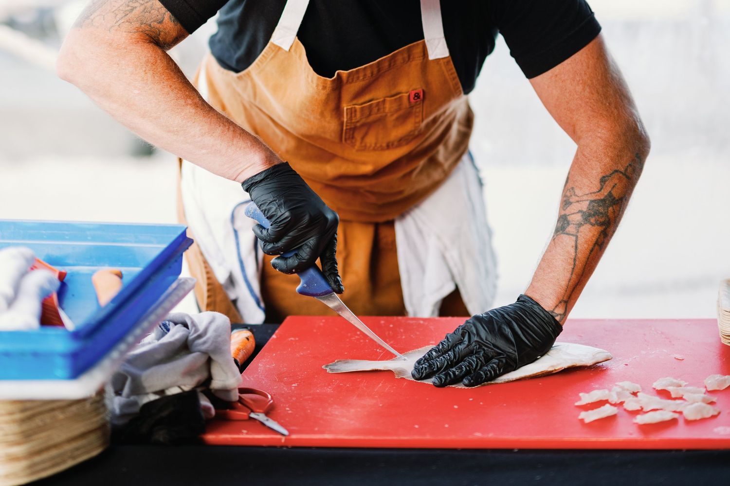 Chef's hands preparing fresh fish on red cutting board in professional kitchen.