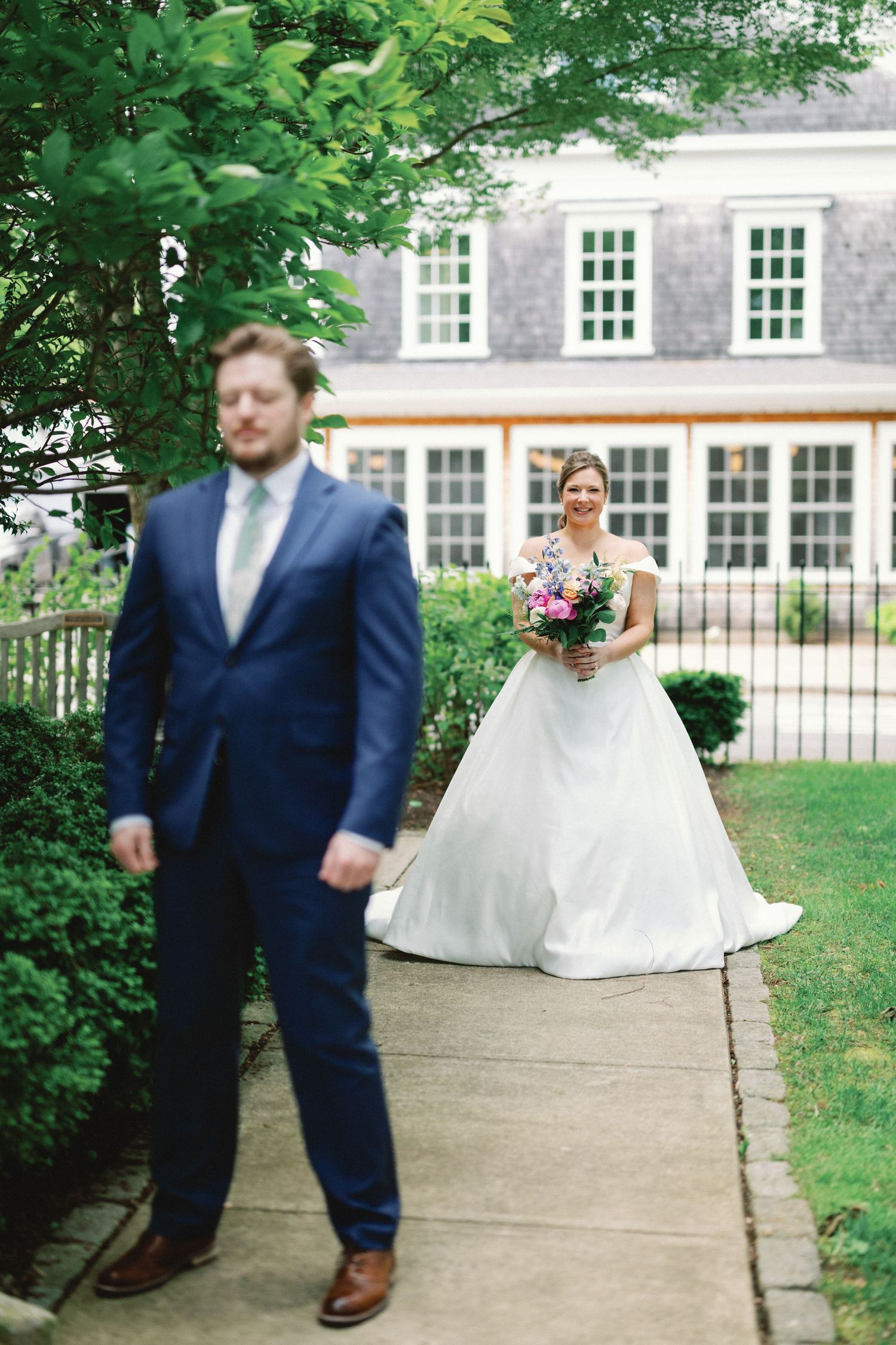 A couple's first look wedding moment captured on a garden pathway with the bride in white and groom in navy suit.
