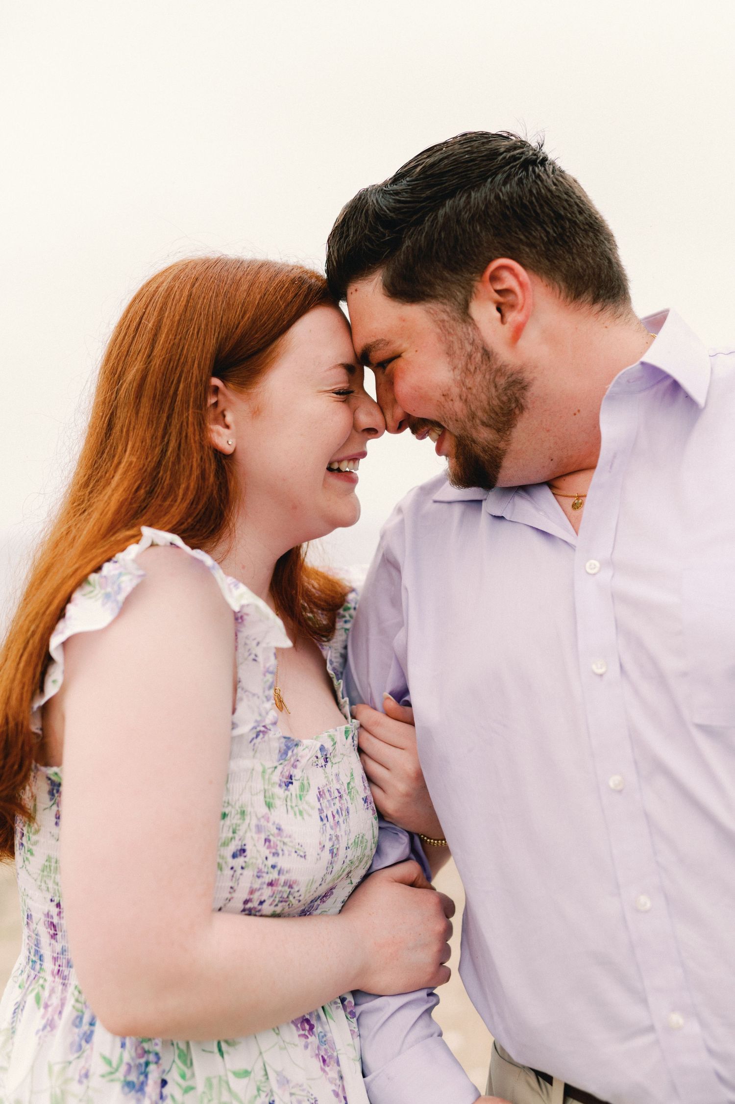 Intimate loving couple sharing a tender moment outdoors, with her wearing a floral dress and him in a light shirt.