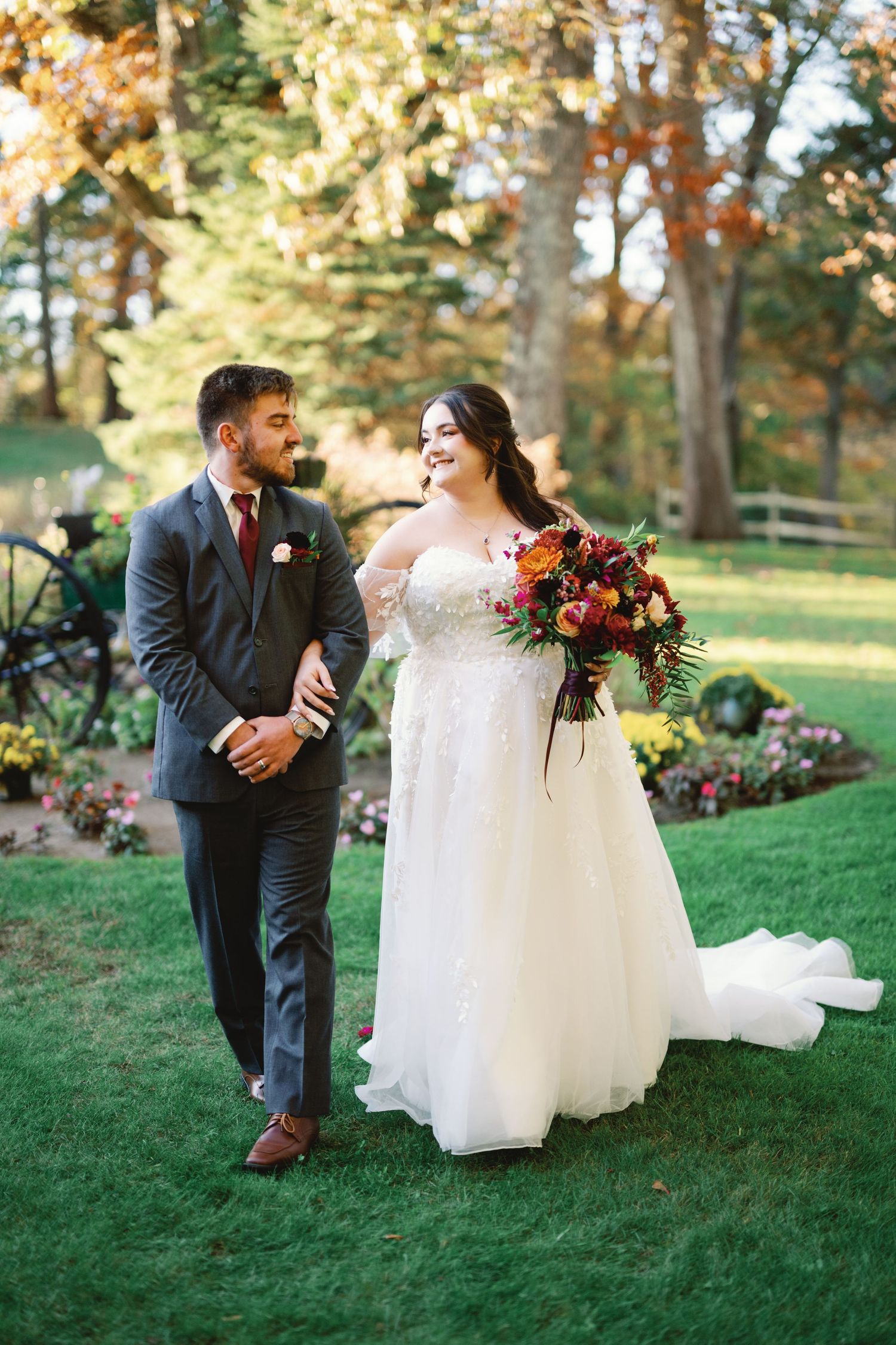 A romantic autumn outdoor wedding scene with newlyweds on a grassy lawn with fall foliage in the background.