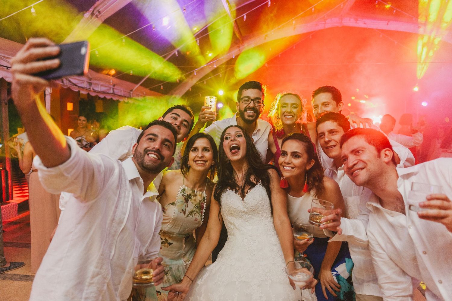Wedding party celebrating on dance floor with vibrant colorful lighting and energetic atmosphere at reception.