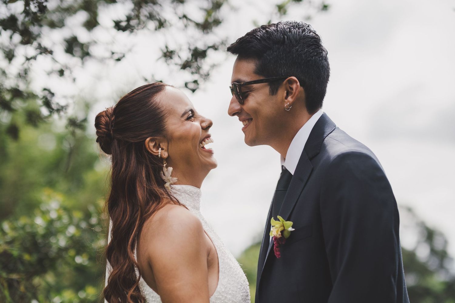 A joyful couple shares a candid moment outdoors during their wedding celebration, with greenery in the background.
