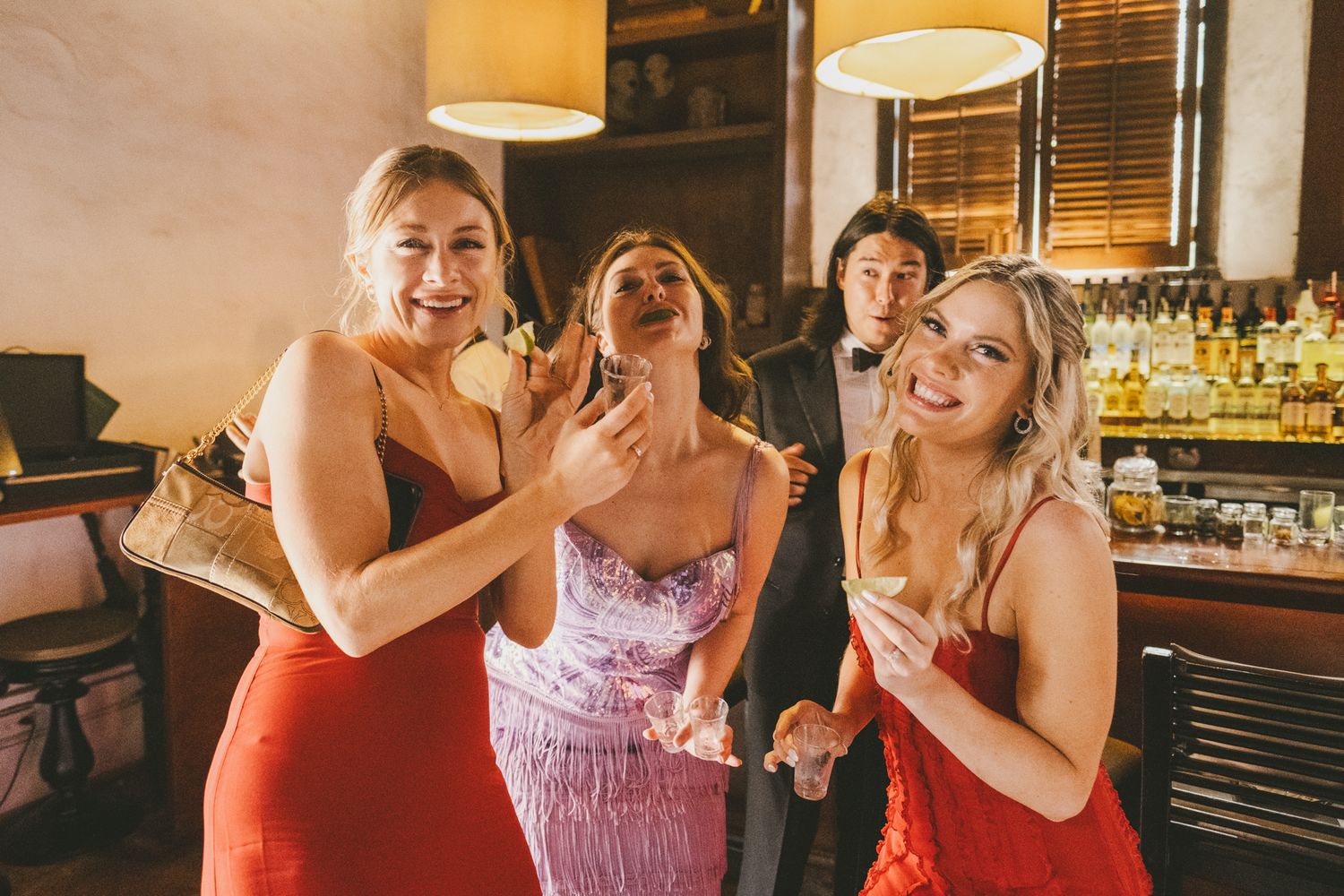 Party guests in red and pink dresses enjoy a fun candid moment together at a bar.