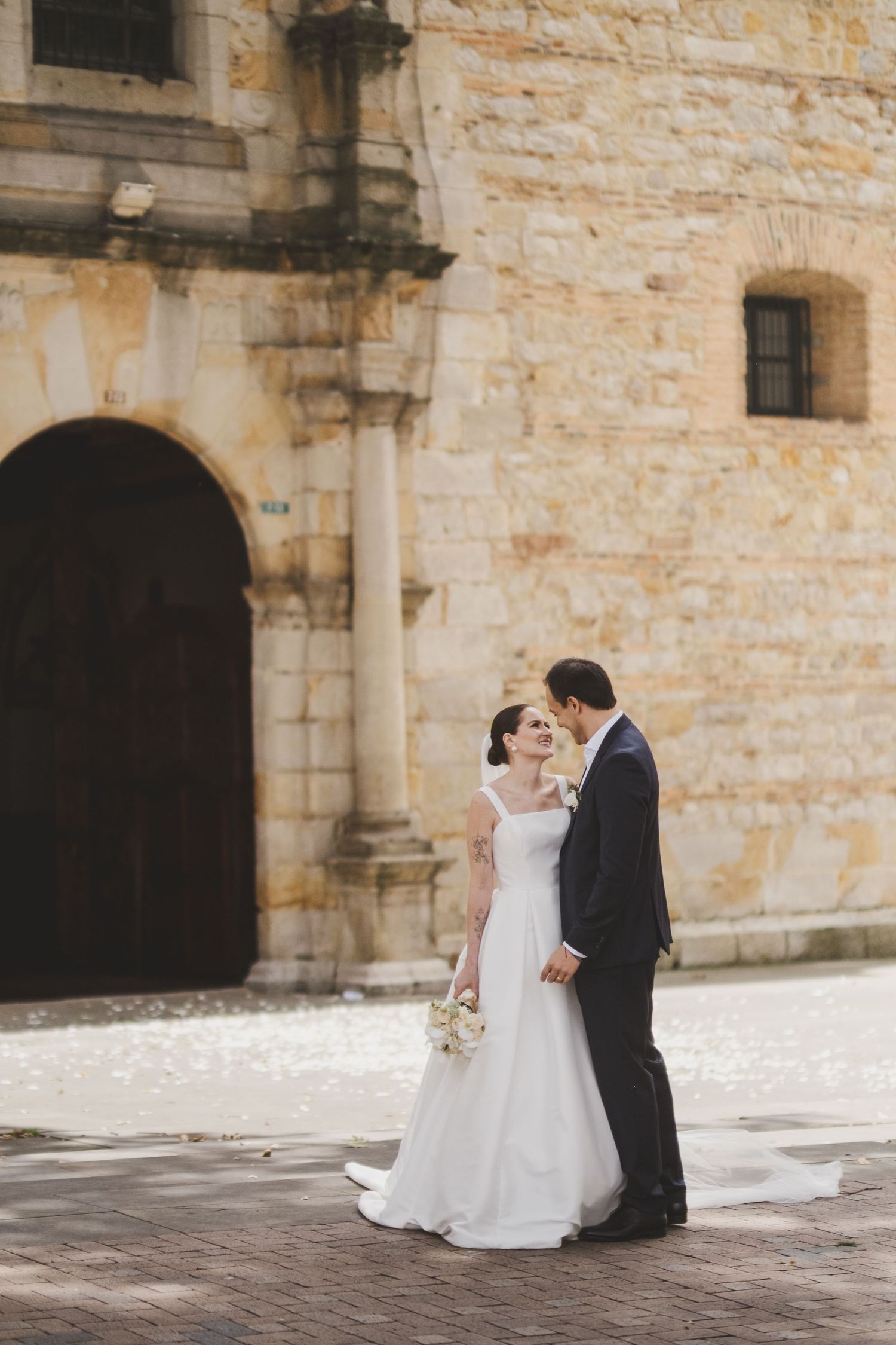 A romantic wedding couple stands outside a historic stone church with arched doorway on their special day.