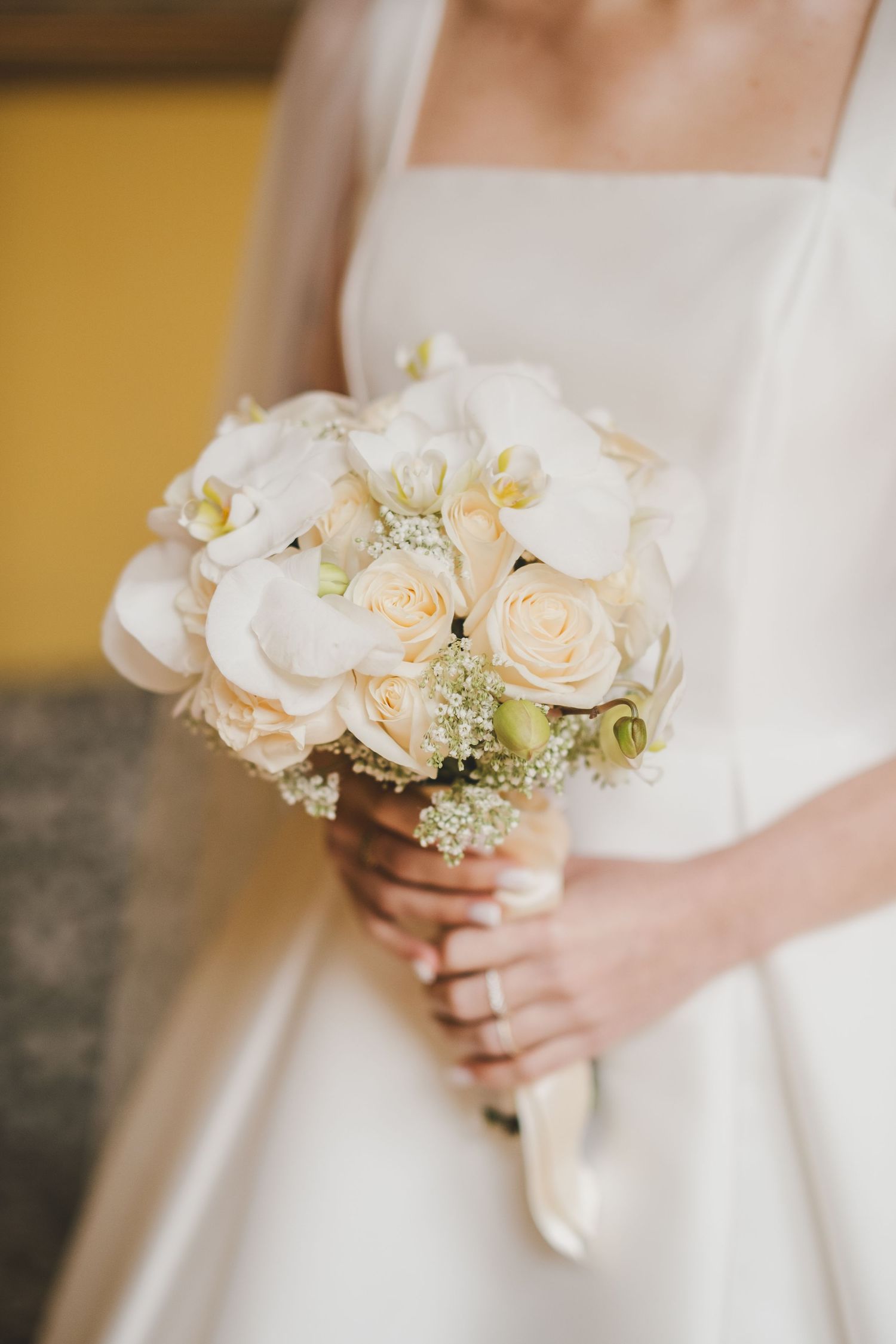Close-up view of delicate white and peach roses in a bridal bouquet with baby's breath accents against a white dress.