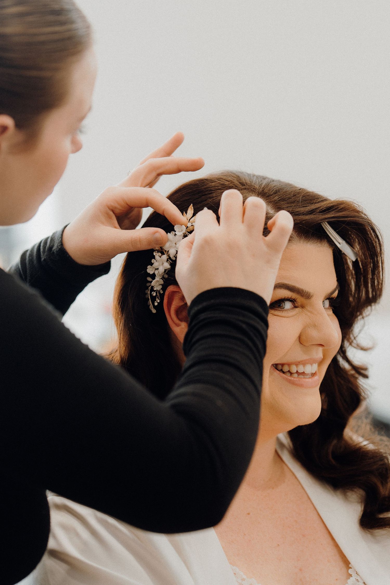 Professional makeup artist gently applying eye makeup on smiling client during bridal beauty preparation.