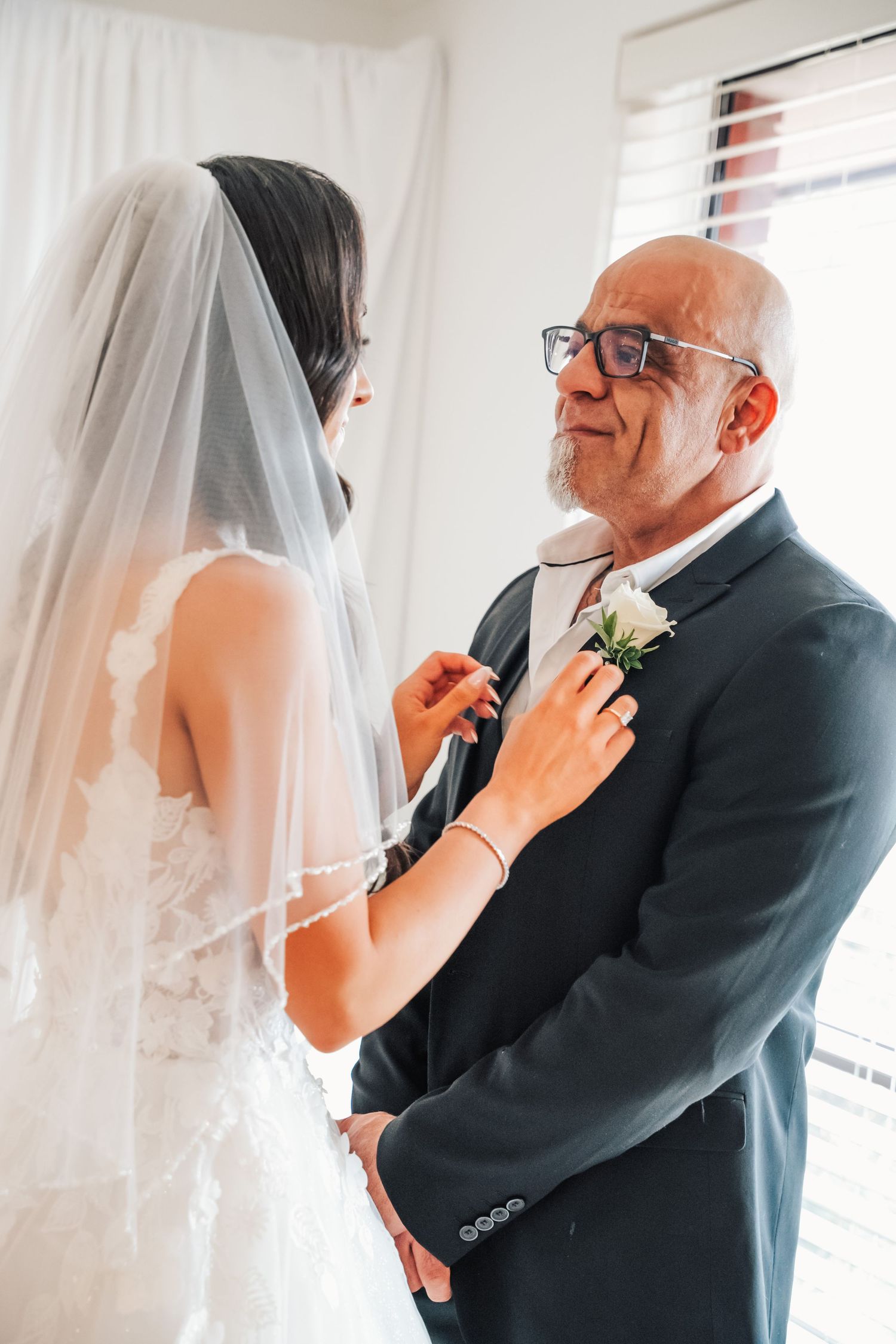 Emotional first look moment between father and daughter on wedding day with flowing veil and window light.