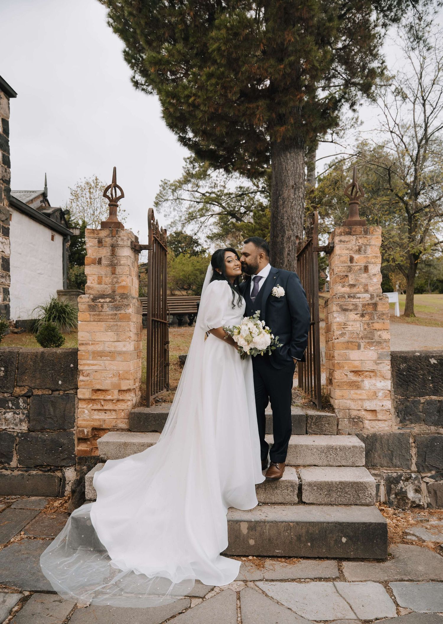 A couple shares an intimate moment at the entrance of a historic stone church gate with a flowing white wedding gown.