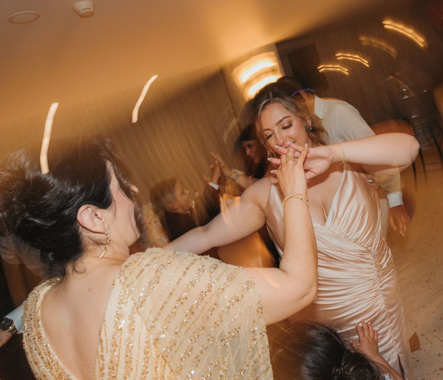 Two people dancing energetically at a party with motion blur and glowing warm lighting in the background.