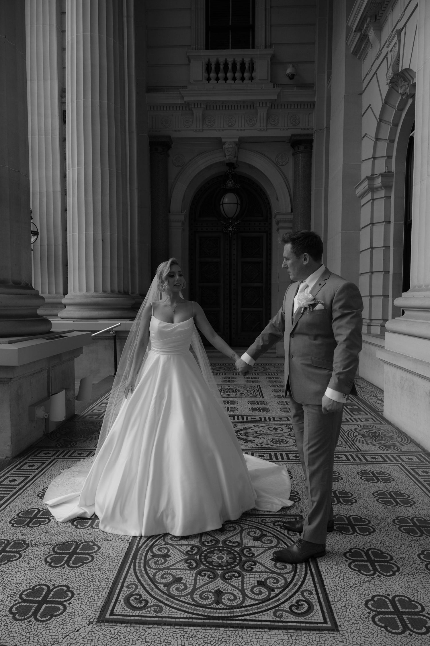 Black and white photo series showing a bride and groom dancing playfully in an ornate hallway with patterned floor tiles.