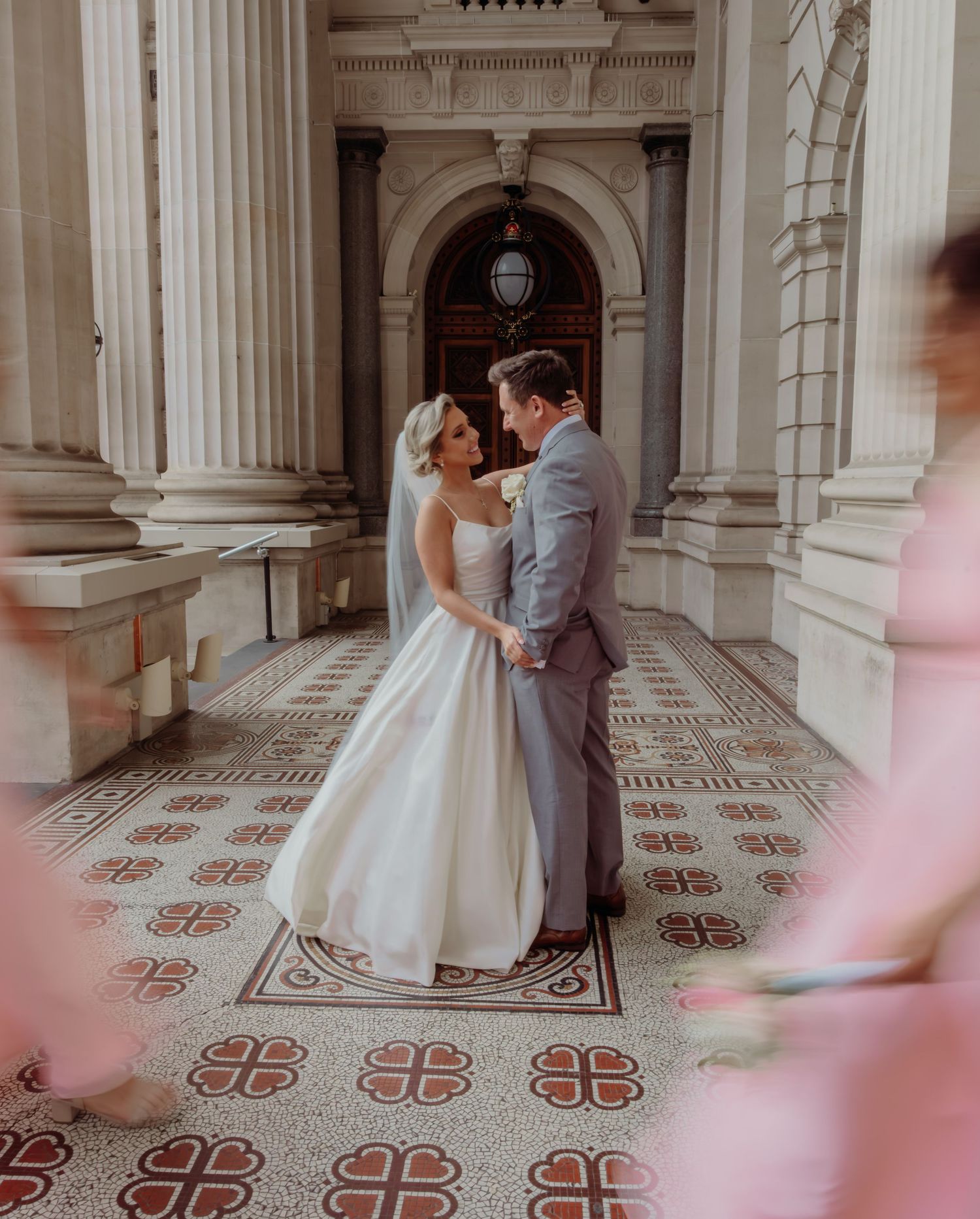Elegant couple shares a romantic moment in ornate hallway with decorative tiled floors and classical architecture.