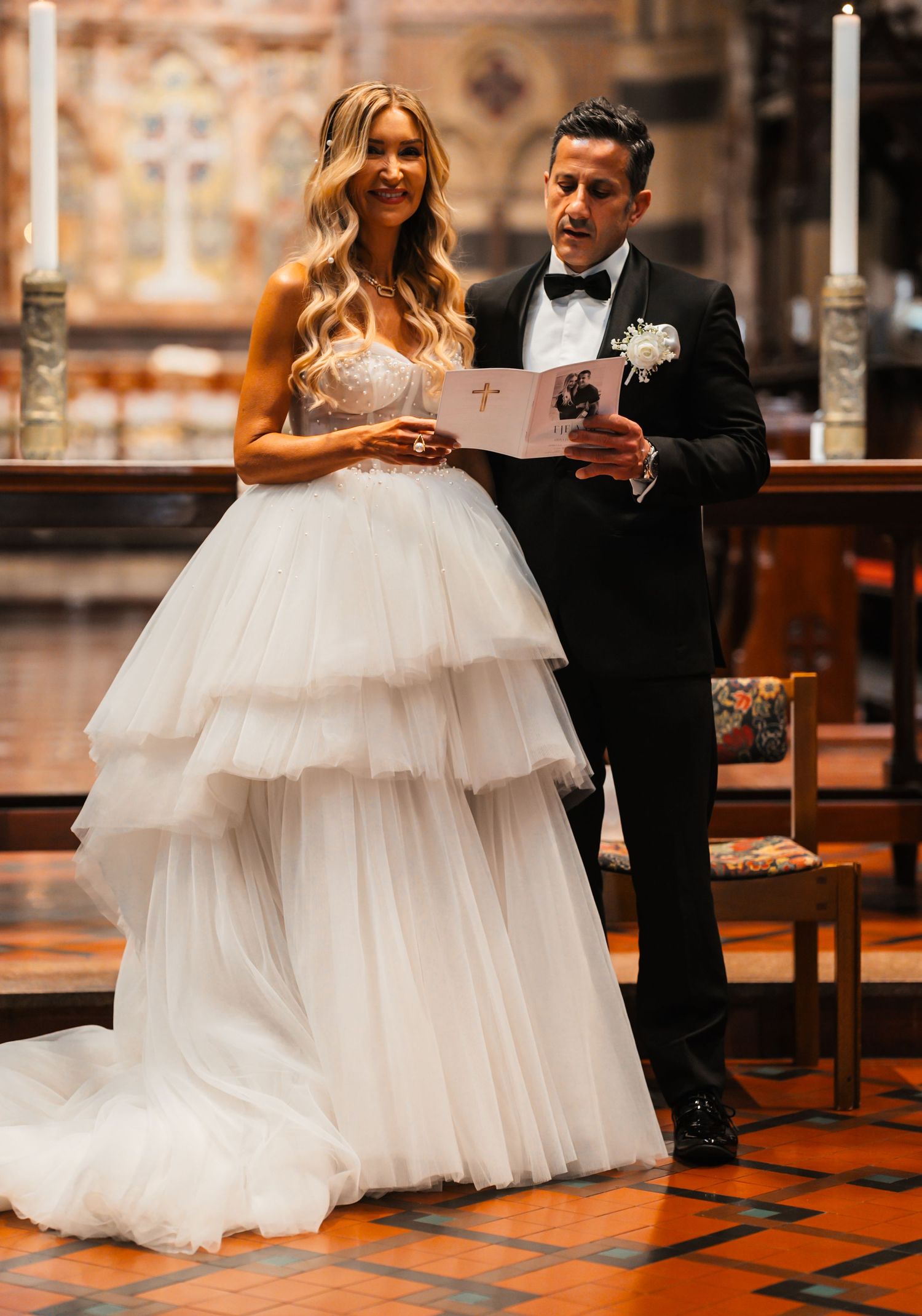 A bride in a layered tulle ballgown and groom in a tuxedo share an intimate moment in a church setting.