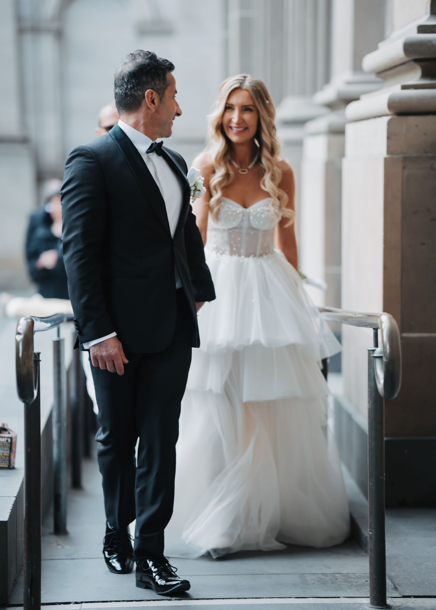 A couple in wedding attire shares a romantic moment in an elegant columned hallway.