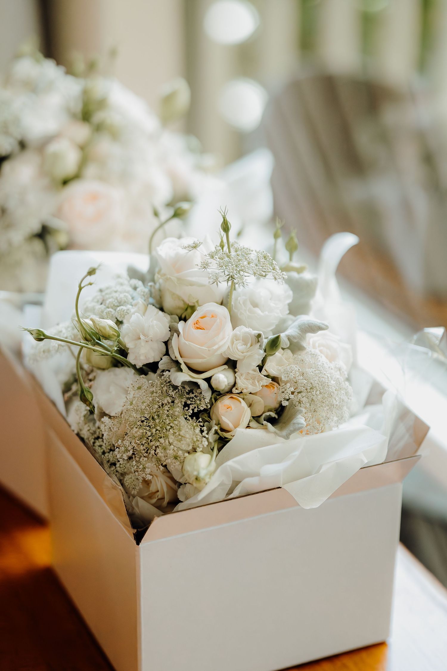 White roses and delicate flowers arranged in elegant white gift boxes create a romantic wedding table setting.