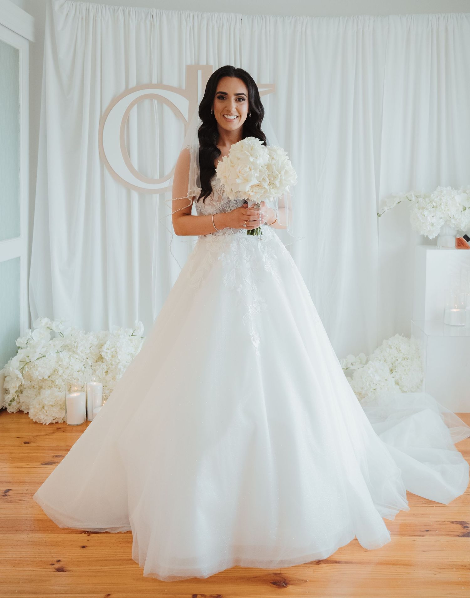 A bride in a flowing white ballgown twirls gracefully on a hardwood floor against a white backdrop.
