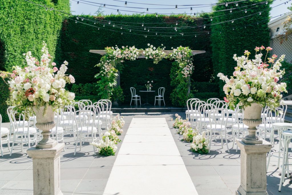 Elegant outdoor wedding reception setup with white chairs and floral arrangements under string lights in a garden setting.
