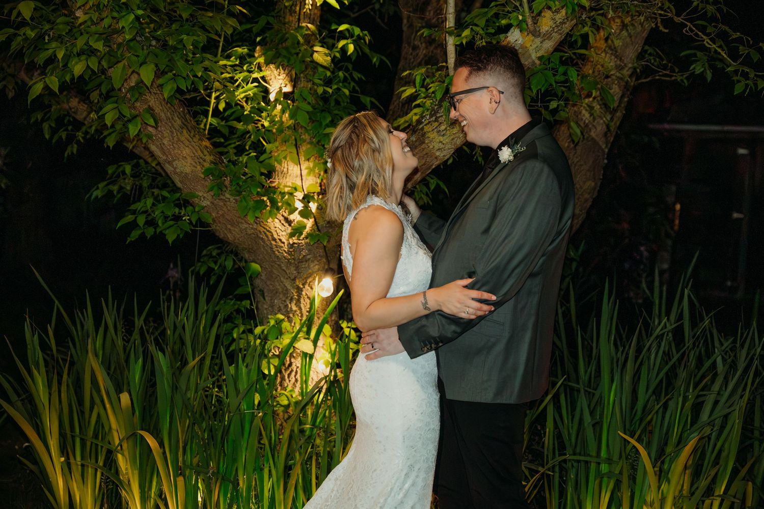 A couple shares a romantic moment in an evening garden setting illuminated by soft outdoor lighting.