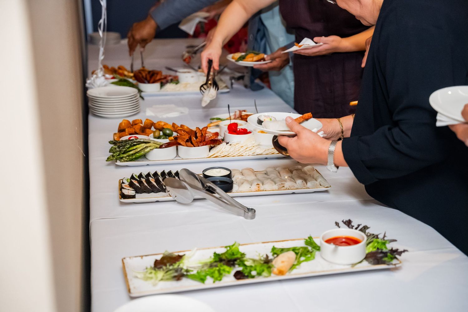 Hands preparing elegant appetizers and sushi platters on white serving boards at an upscale catering event.