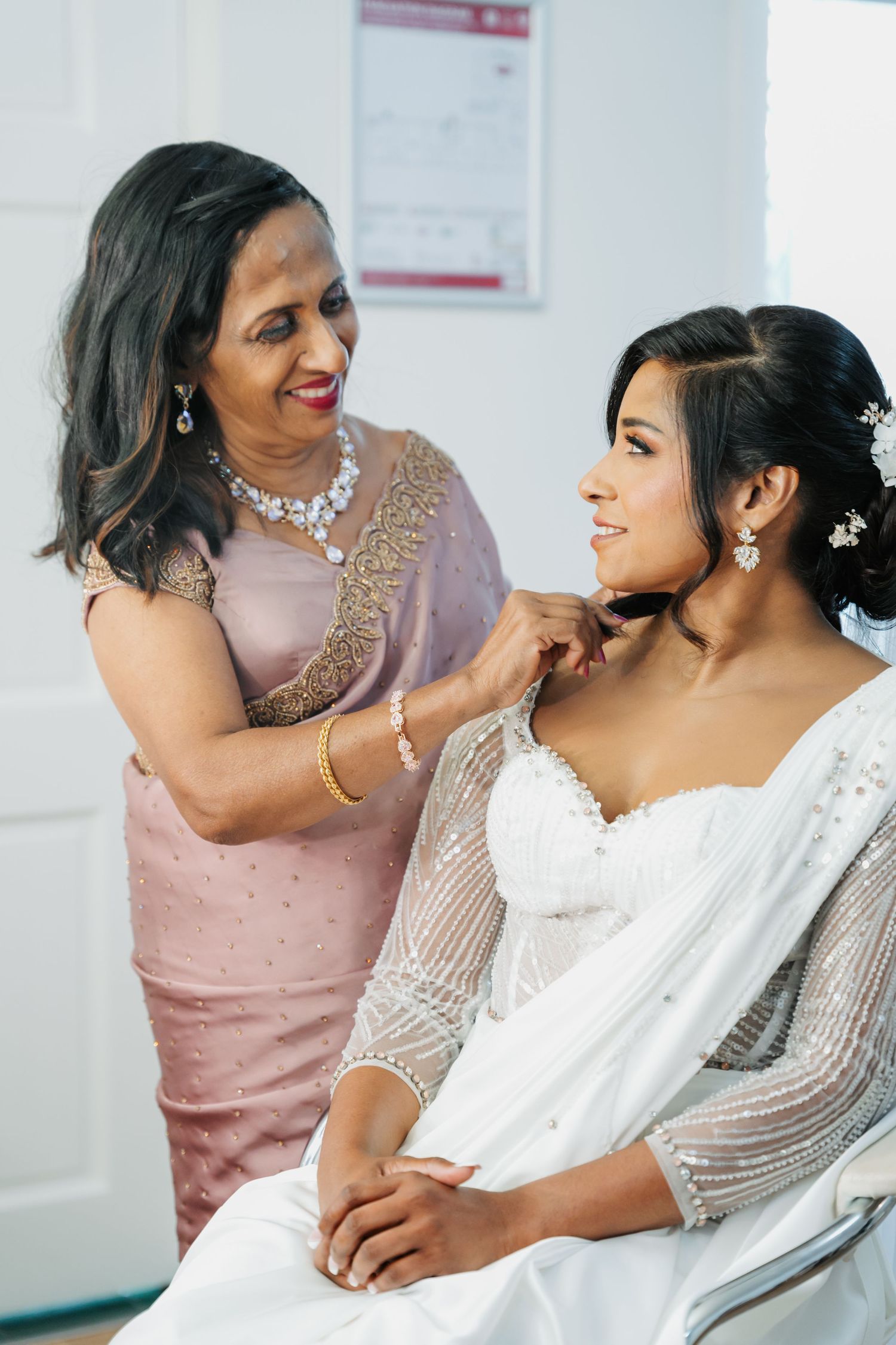 A tender moment between mother and bride on wedding day as they prepare in a light-filled room.