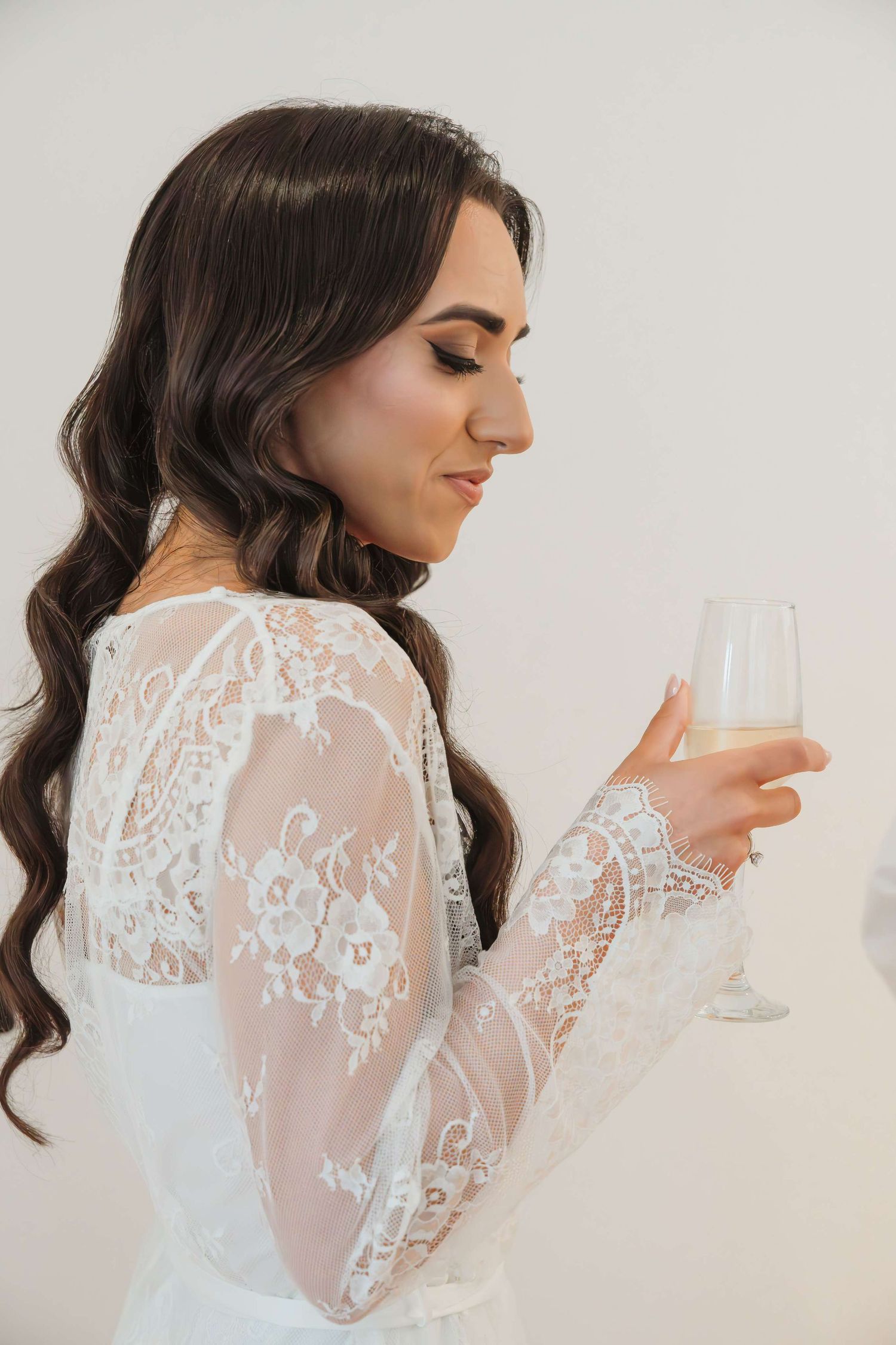 A profile view of a bride in a white lace sleeve wedding dress holding a champagne glass.