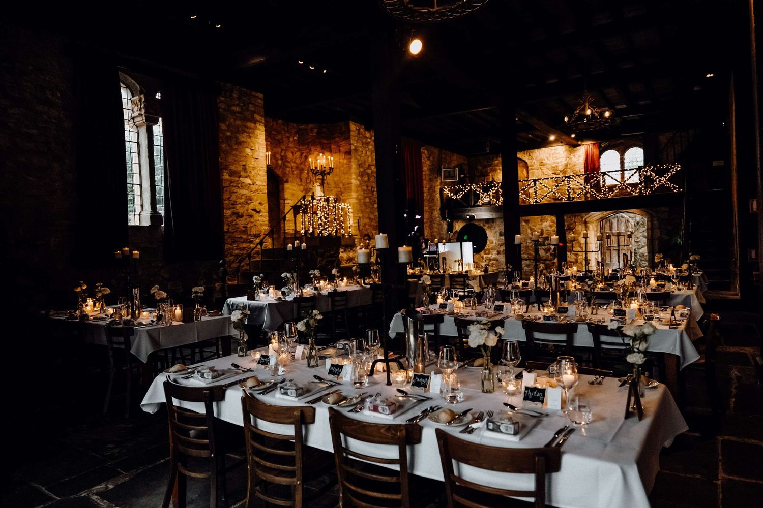 Elegant wedding reception setup in a rustic venue with long tables, white linens, and warm ambient lighting.