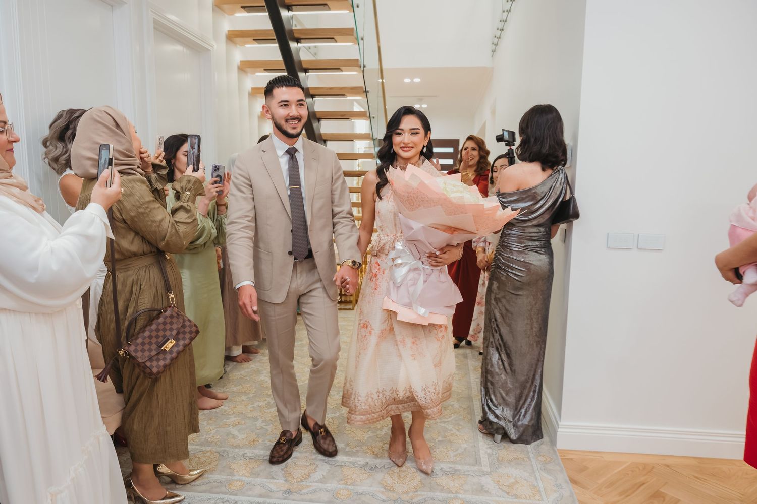Wedding party members in neutral beige and tan attire pose together during outdoor celebration.