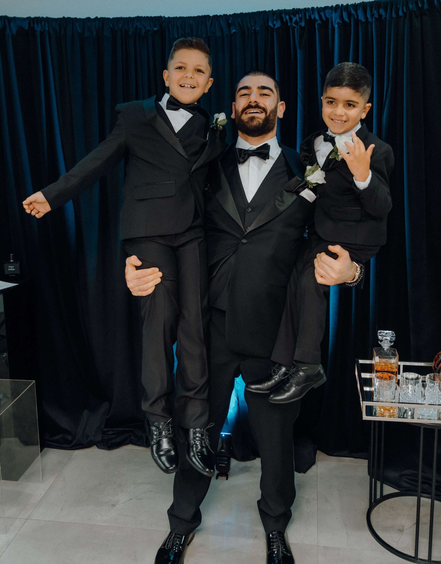 Wedding party members in black tuxedos having fun with playful poses during formal photo session.