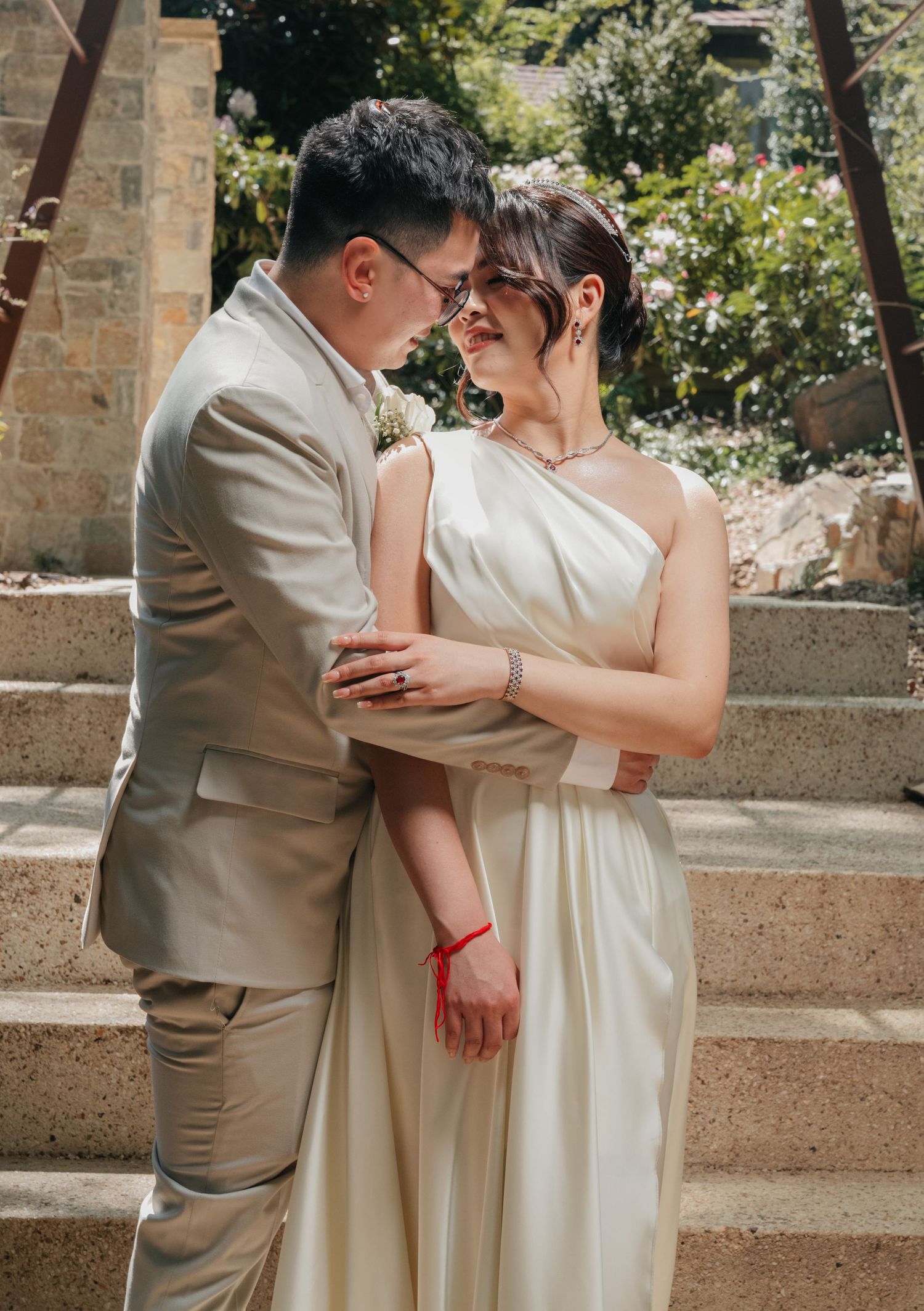 A romantic bridal couple shares an intimate moment on stone steps surrounded by lush garden foliage.